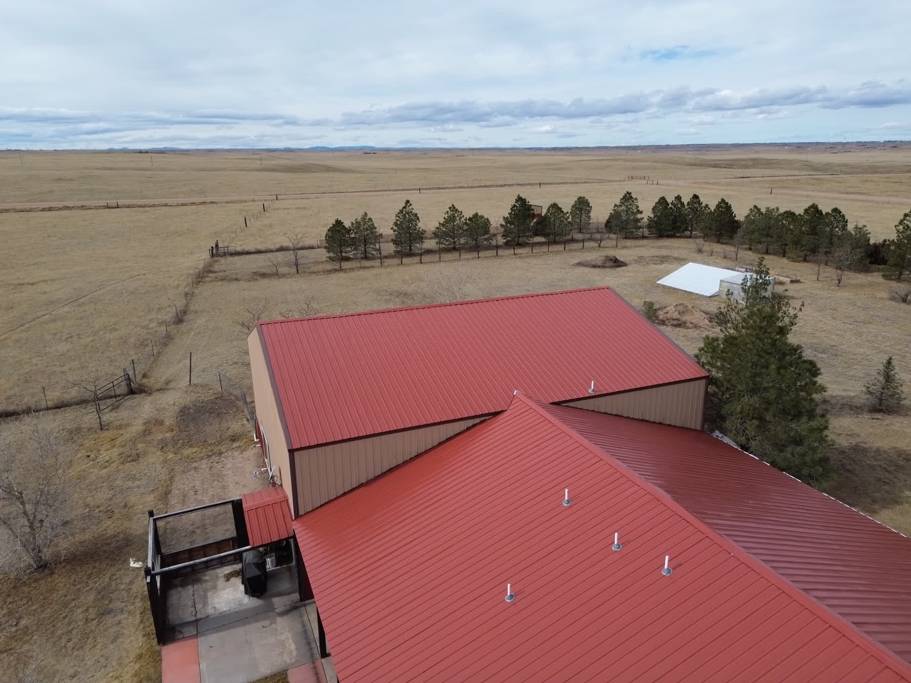 Drone view of a red metal-roofed ranch complex and nearby outbuilding