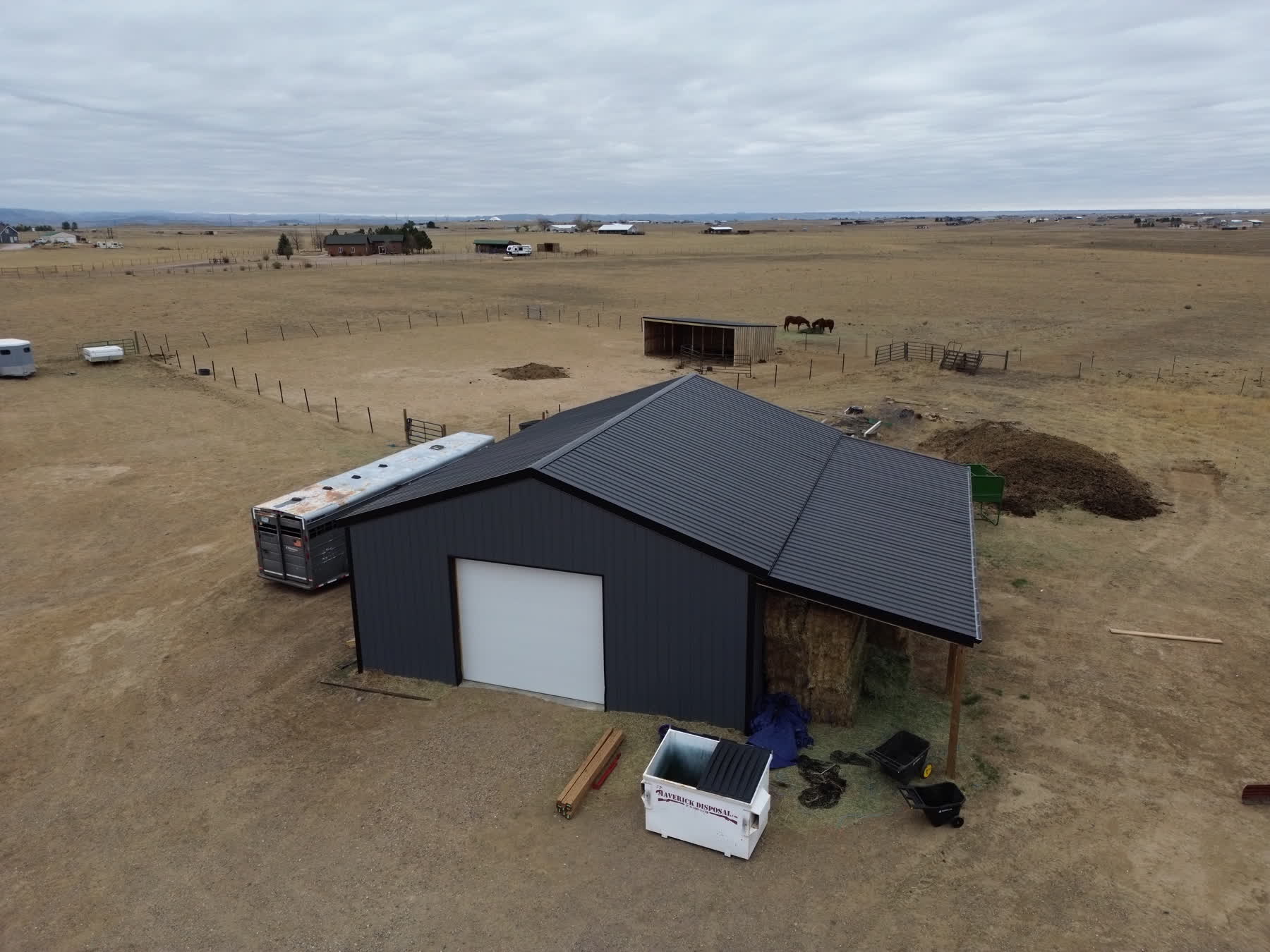 Drone view of a dark metal-roofed barn with the surrounding ranch property