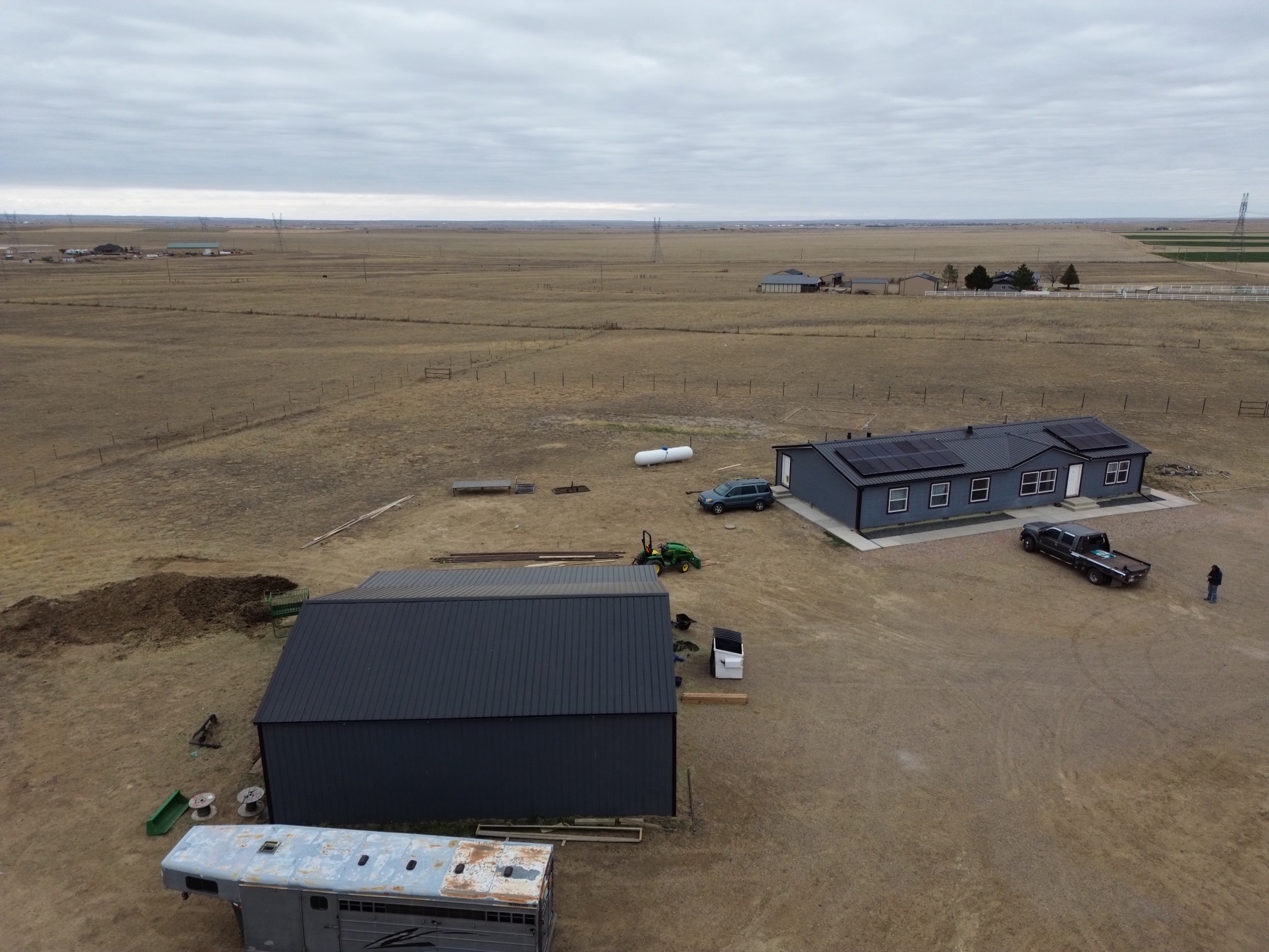Drone view of a finished dark-roofed home and large outbuilding